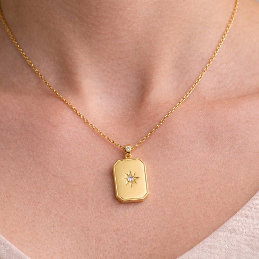 Gold necklace with a pendant on a person wearing a light pink top.