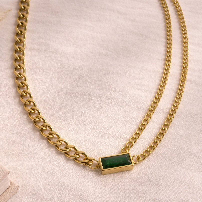 Gold chain necklace with a green gemstone on a light background