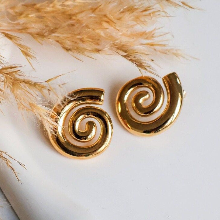 Gold spiral earrings on a white surface with dried grasses in the background