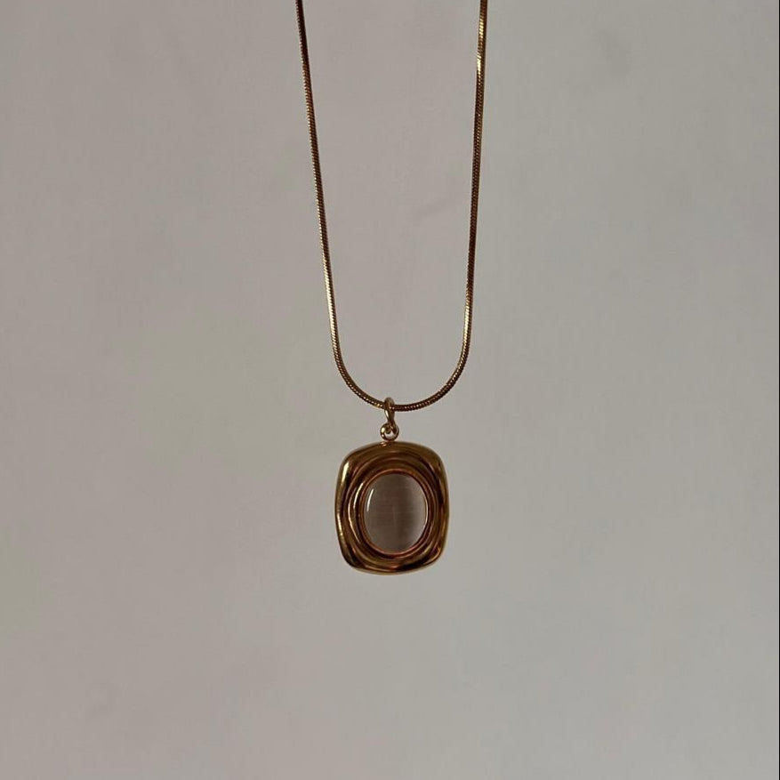 Gold necklace with a square pendant on a plain background