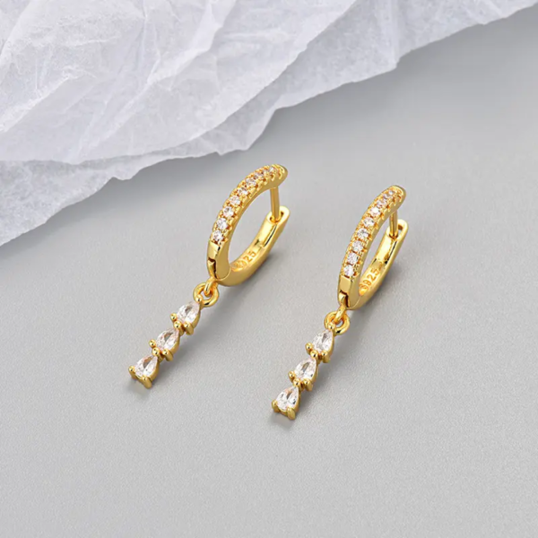 Gold hoop earrings with dangling crystals on a gray surface
