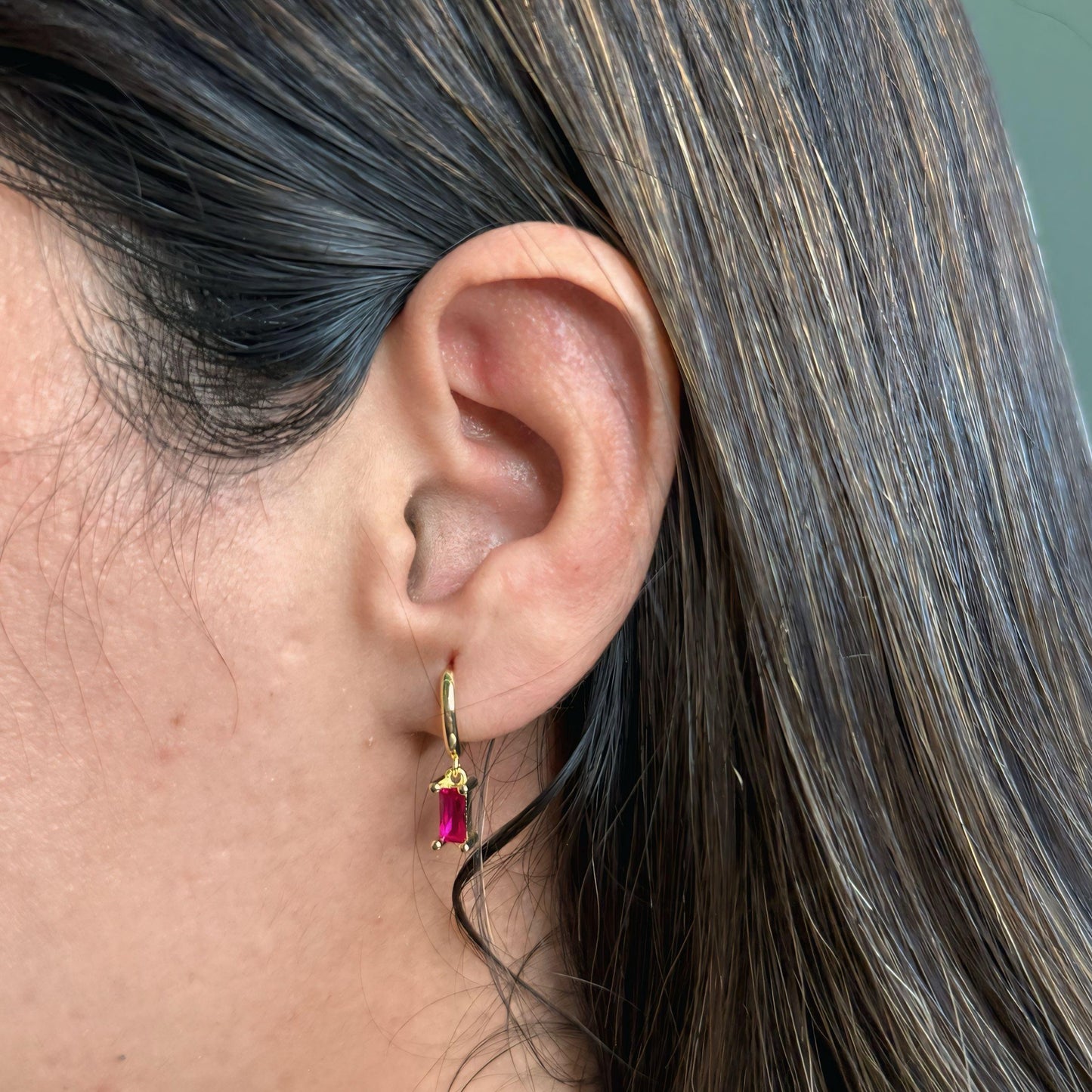 Close-up of an ear wearing a gold earring with a red gemstone against a blurred background