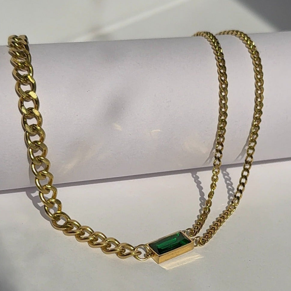 Gold chain necklace with a green gemstone pendant on a white surface