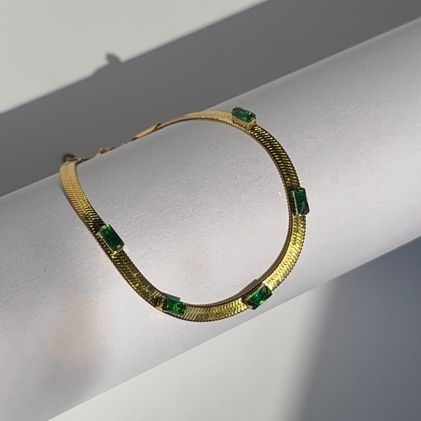 Gold necklace with green gemstones on a white background