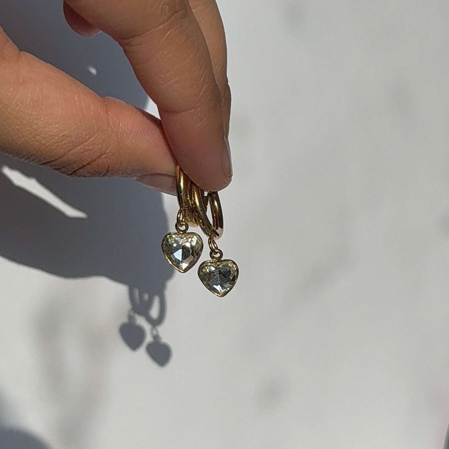 Gold earring with heart-shaped charms held by a hand against a white background