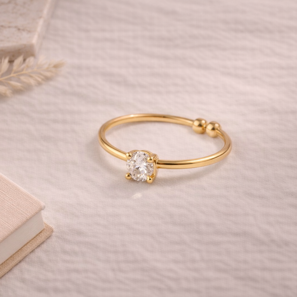 Gold ring with a diamond on a textured surface with a book and decorative leaf.
