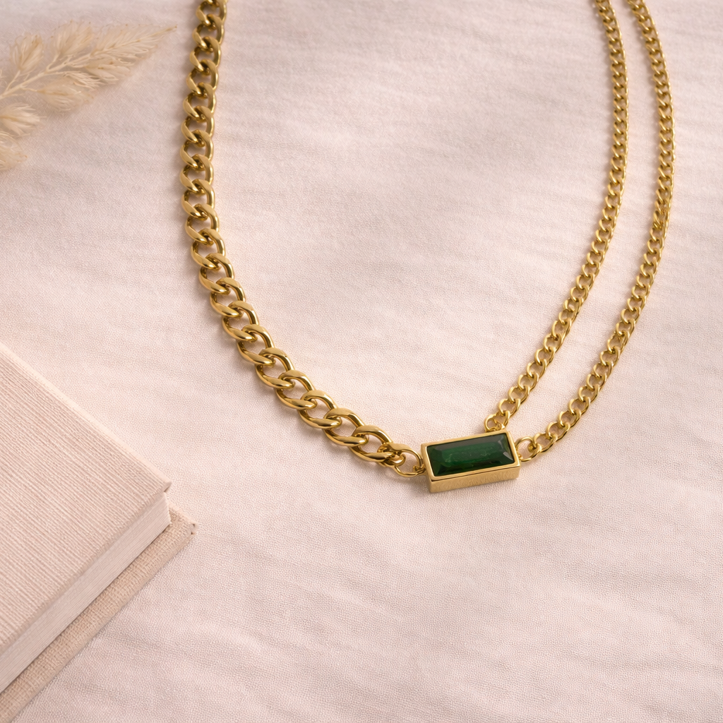 Gold chain necklace with a green gemstone on a light background