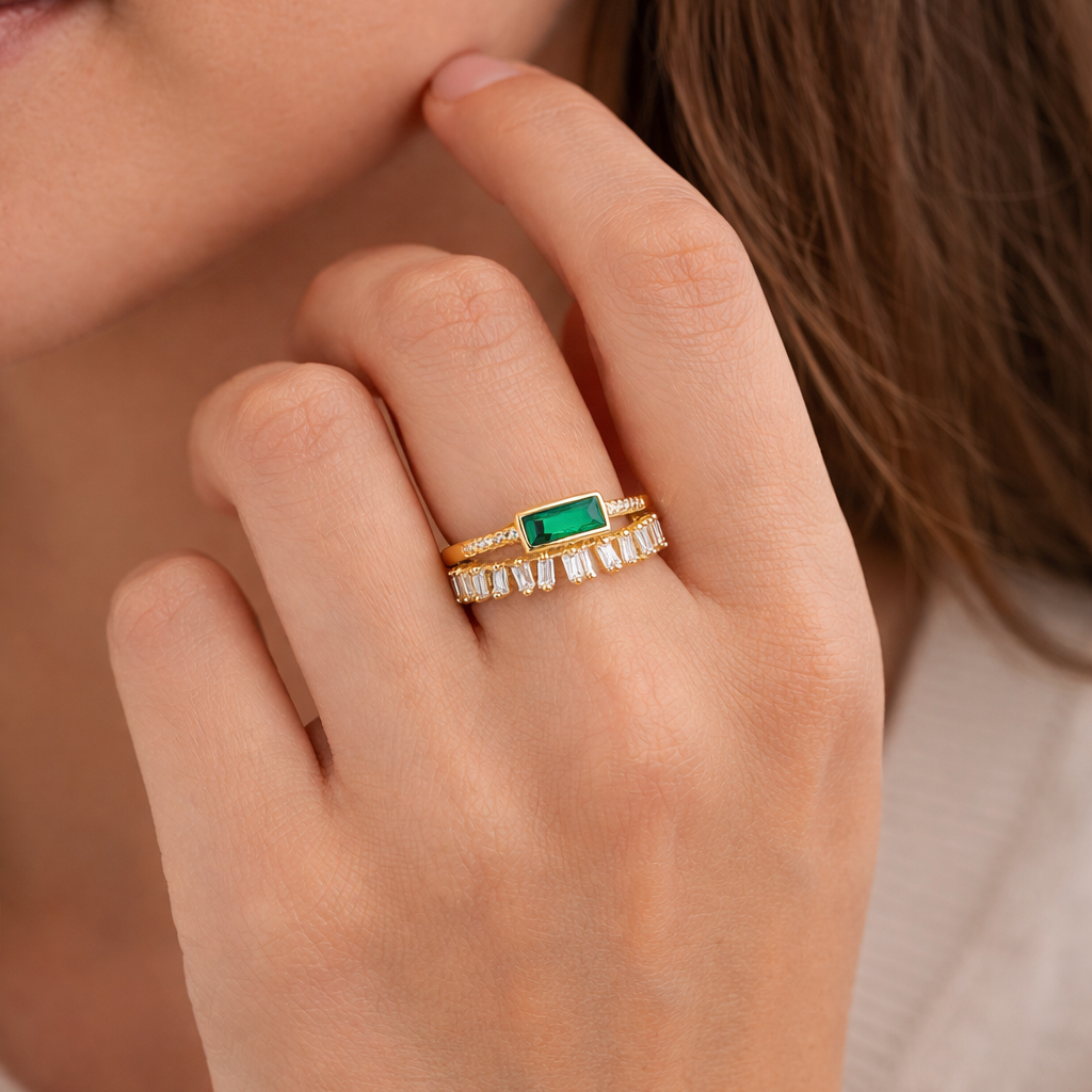 Close-up of a hand wearing two rings with a green gemstone and diamond accents.
