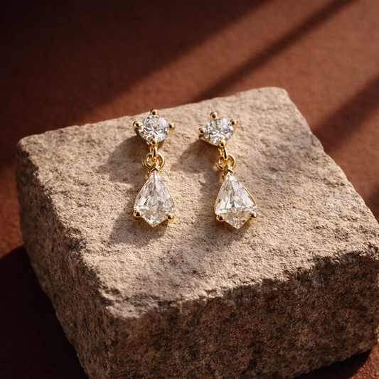 Gold earrings with clear gemstones on a textured stone surface