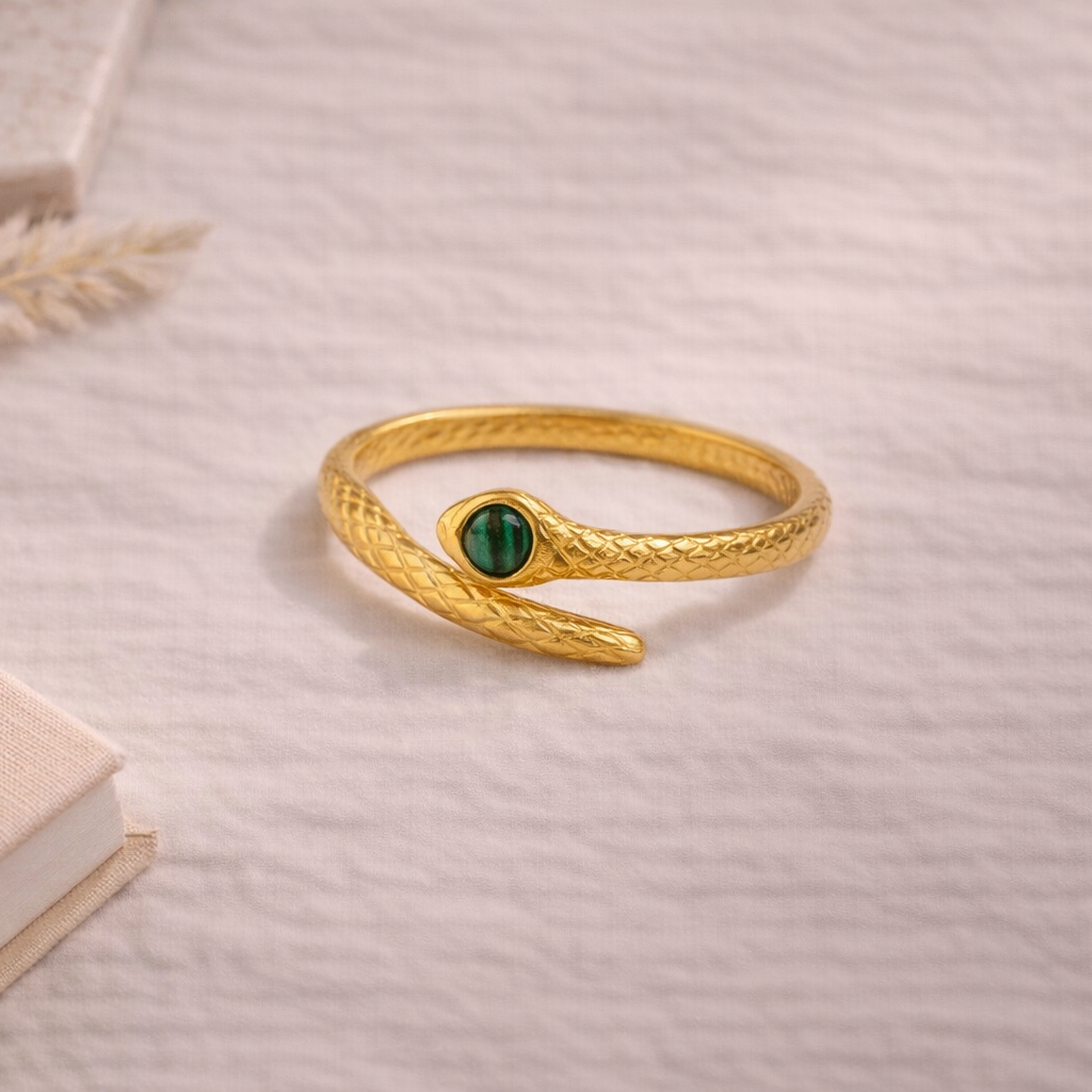 Gold snake-shaped ring with a green gemstone on a light background