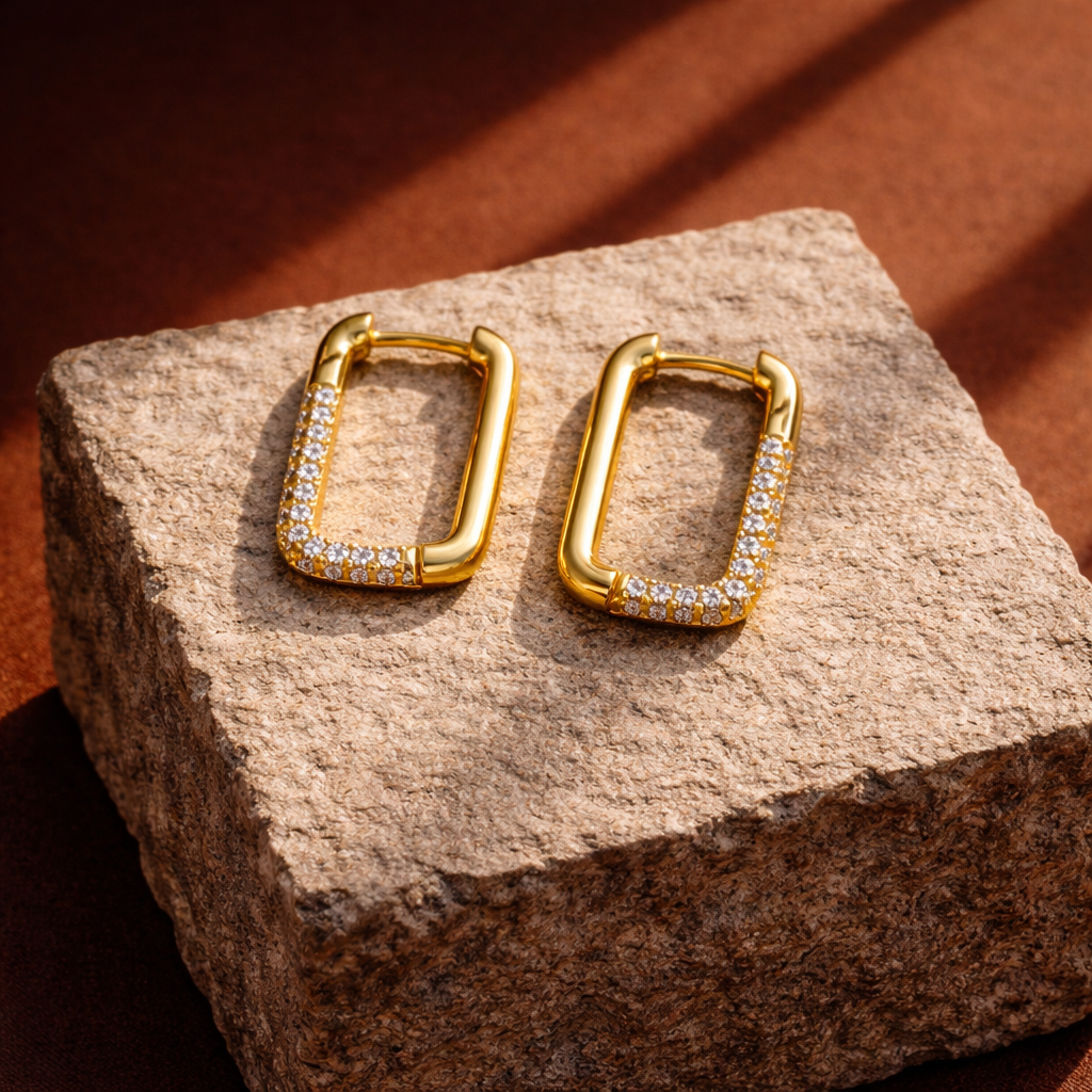 Gold hoop earrings with embedded stones on a textured stone surface