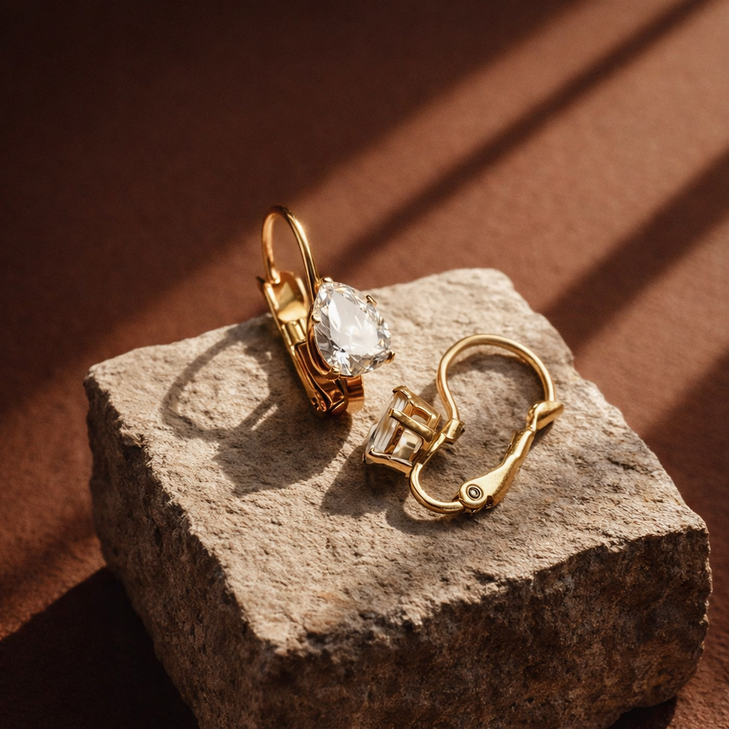 Gold earrings with clear gemstones on a textured stone surface