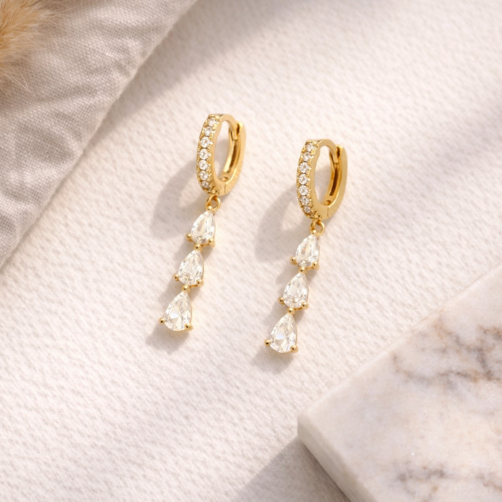 Gold earrings with pearl drops on a marble surface