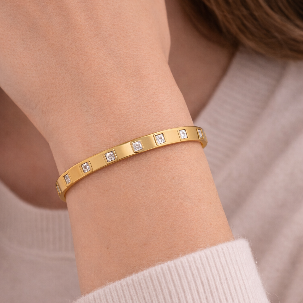 Gold bracelet with small diamonds on a person's wrist against a neutral background