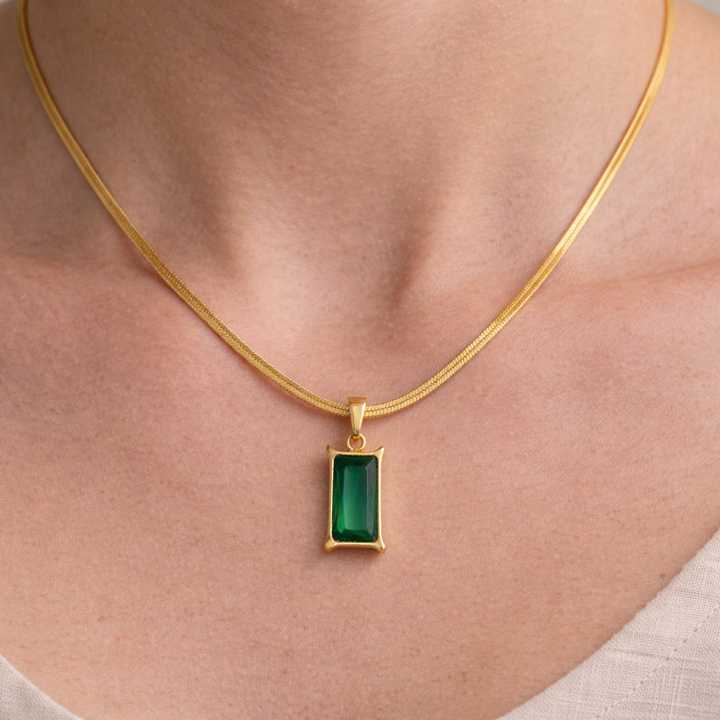 Gold necklace with a green pendant on a person wearing a beige top.