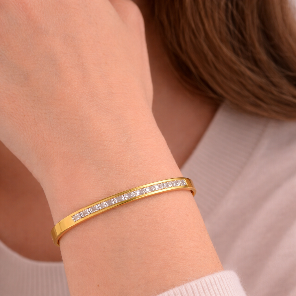 Gold bracelet with small stones on a person's wrist against a neutral background