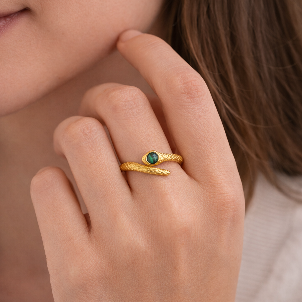 Close-up of a hand wearing a gold ring with a green gemstone, against a neutral background.