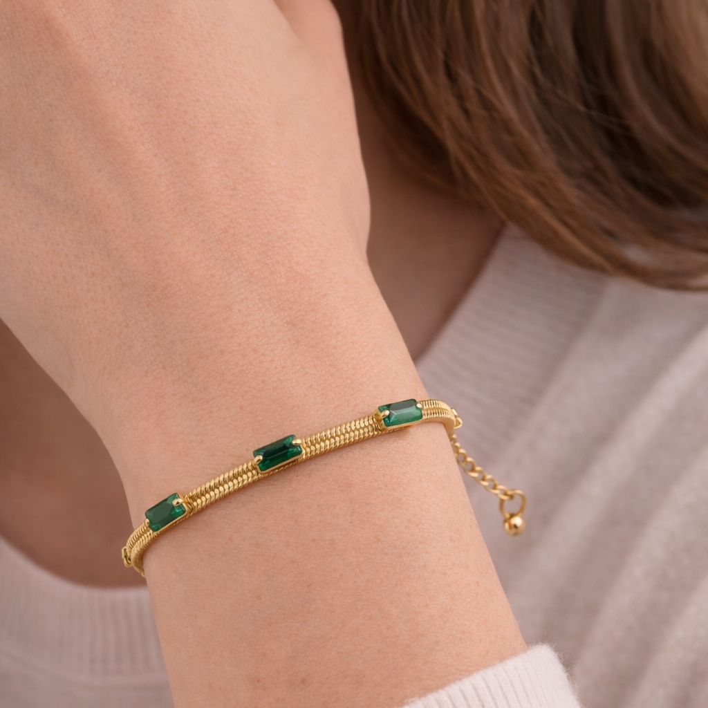 Gold bracelet with green gemstones on a person's wrist against a neutral background