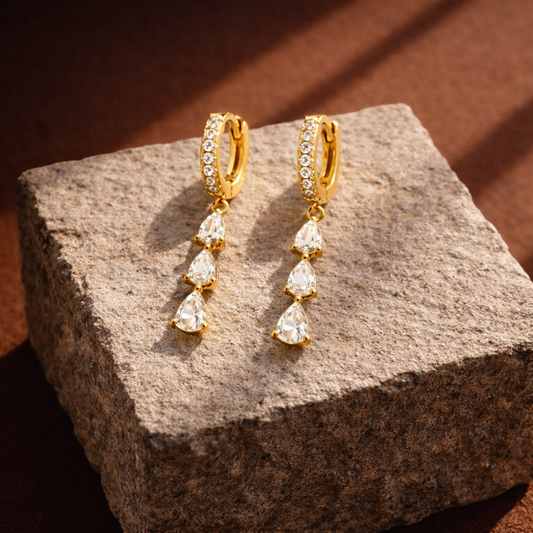 Gold earrings with clear stones on a textured stone surface