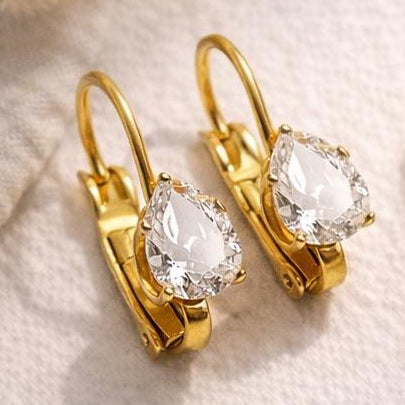 Gold earrings with clear gemstones on a light fabric background