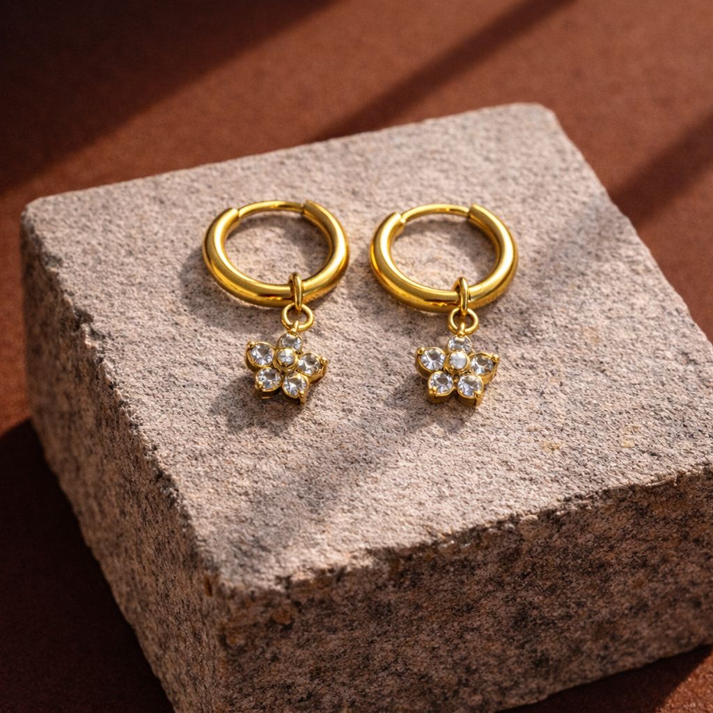 Gold hoop earrings with paw print charms on a textured stone surface