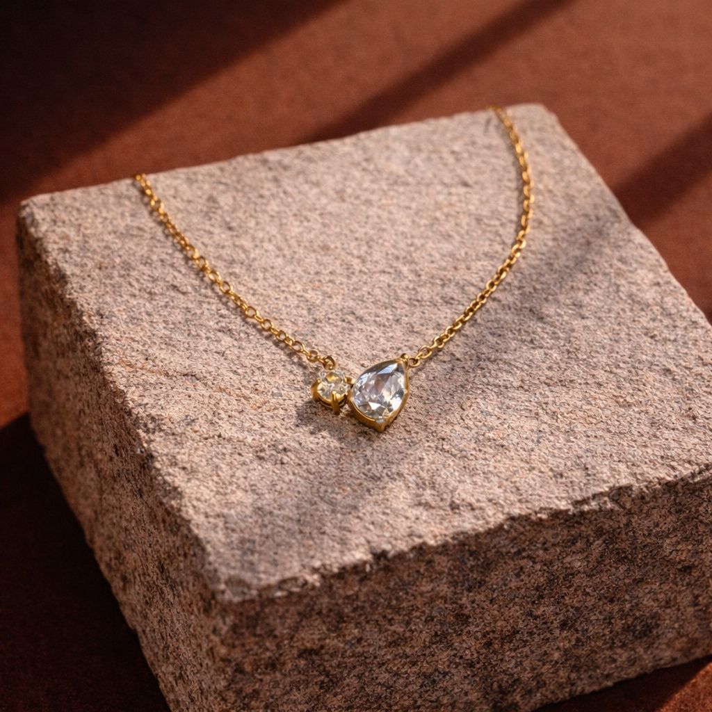 Gold necklace with a teardrop-shaped pendant on a textured stone surface