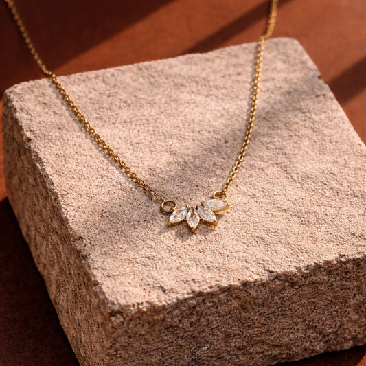 Gold necklace with leaf-shaped pendant on a textured stone surface